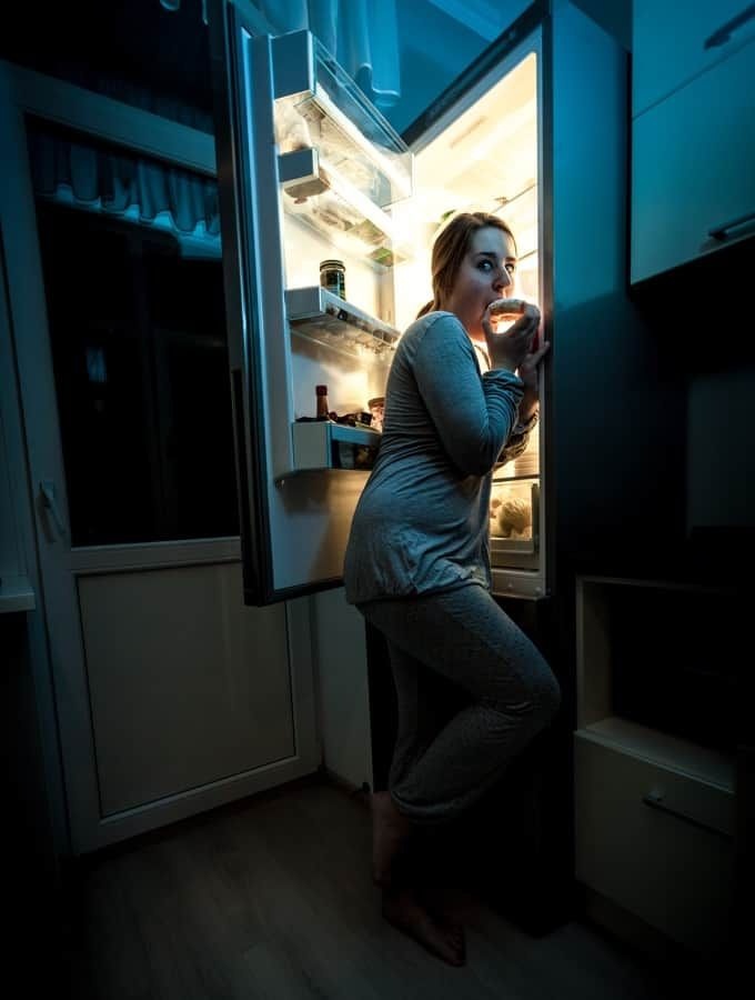 Person standing at an open refrigerator late at night during a craving